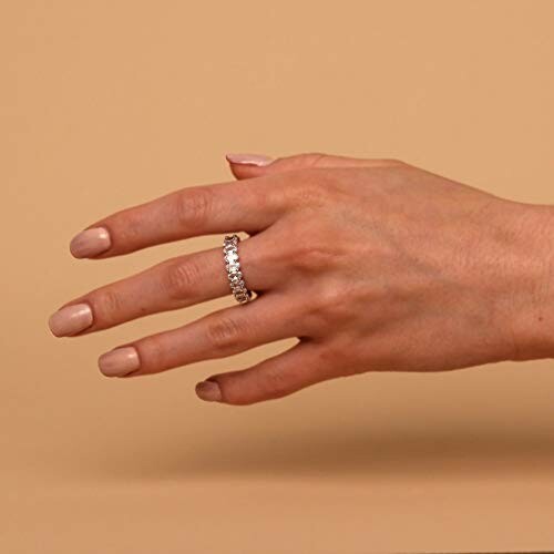 A hand wearing a diamond ring against a beige background.