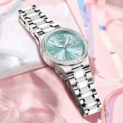 Luxury silver watch with blue dial on pink background.