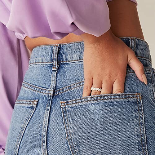 A woman's hand with rings in the back pocket of jeans.