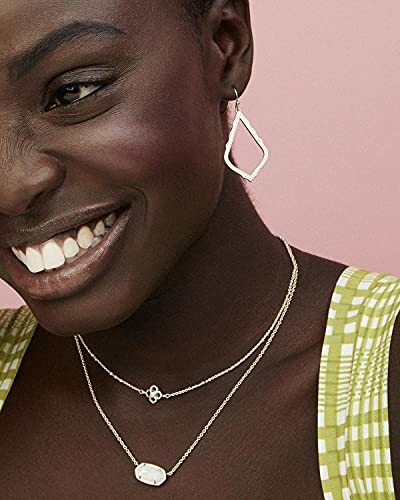 Woman smiling, wearing silver earrings and layered necklaces.