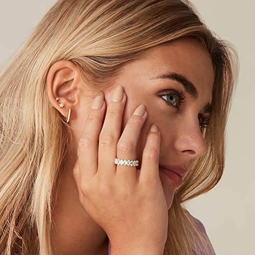 A woman wearing earrings and a ring, resting her face on her hand.